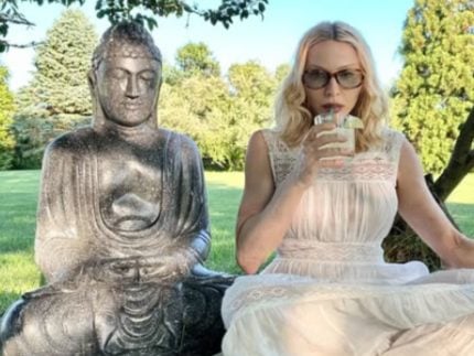 fazendo-carao-com-um-drink-na-mao-ao-lado-de-uma-estatua-de-buda,-madonna-critica-trump