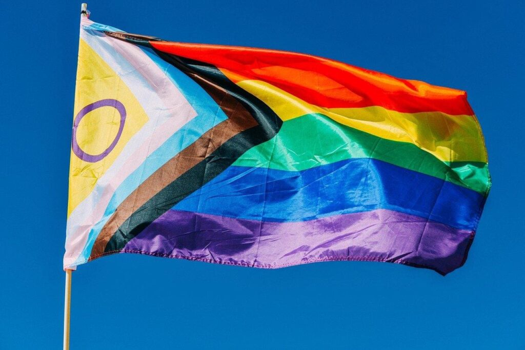 Bandeira do orgulho LGBTQIAPN+ com cores do arco-íris sendo exibida em ambiente urbano, símbolo de diversidade, inclusão e luta por direitos.