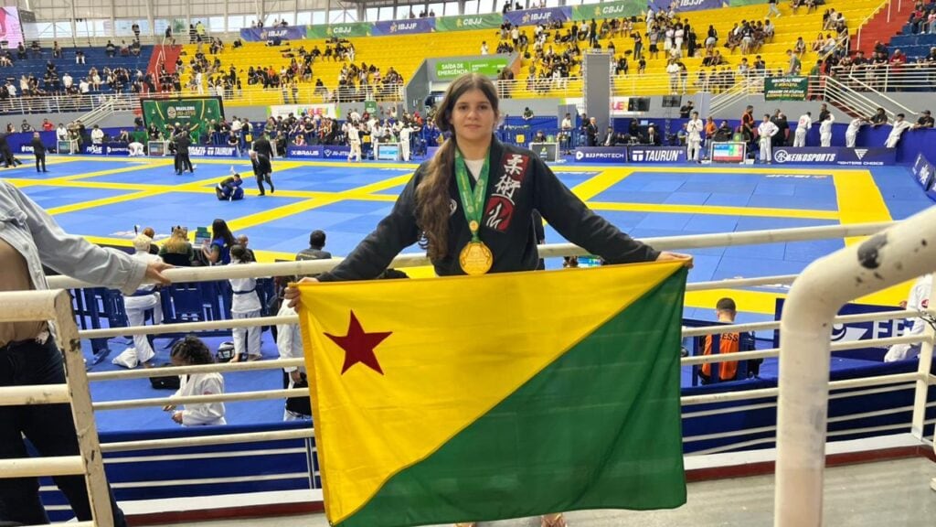 Atleta acreana com medalha de ouro e bandeira acreana em campeonato de jiu-jitsu.