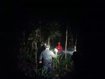 Equipes de resgate e familiares realizando buscas em área rural e de vegetação às margens de rio