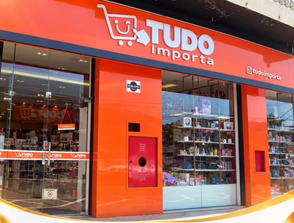 Fachada e interior da loja Tudo Importa com prateleiras de produtos e cartazes de promoção de aniversário.
